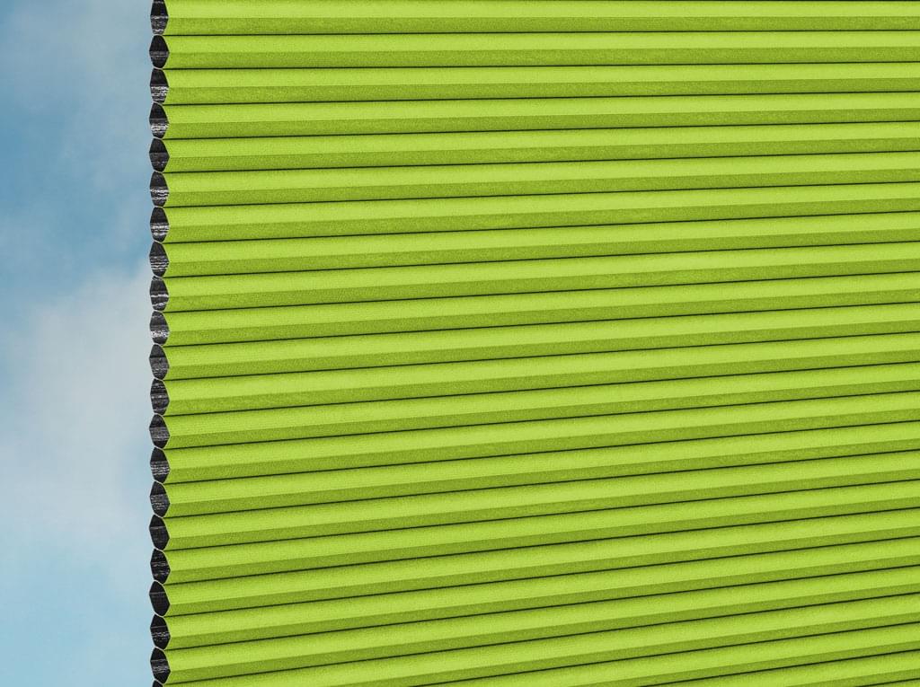 Nahaufnahme der DUETTE® Fixé Unix Dark (3.7472) Grün Jalousien von Duetteshop mit einem Wabenmuster, das teilweise einen strahlend blauen Himmel und sanfte Wolken im Hintergrund zeigt.