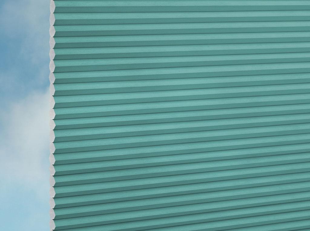 Eine Nahaufnahme von DUETTE® Fixé FR (2.7240) Türkis von Duetteshop zeigt ein tealfarbenes, horizontal plissiertes Rollo mit weichem Tageslicht und einem teilweise bewölkten Himmel, der am linken Rand sichtbar ist.