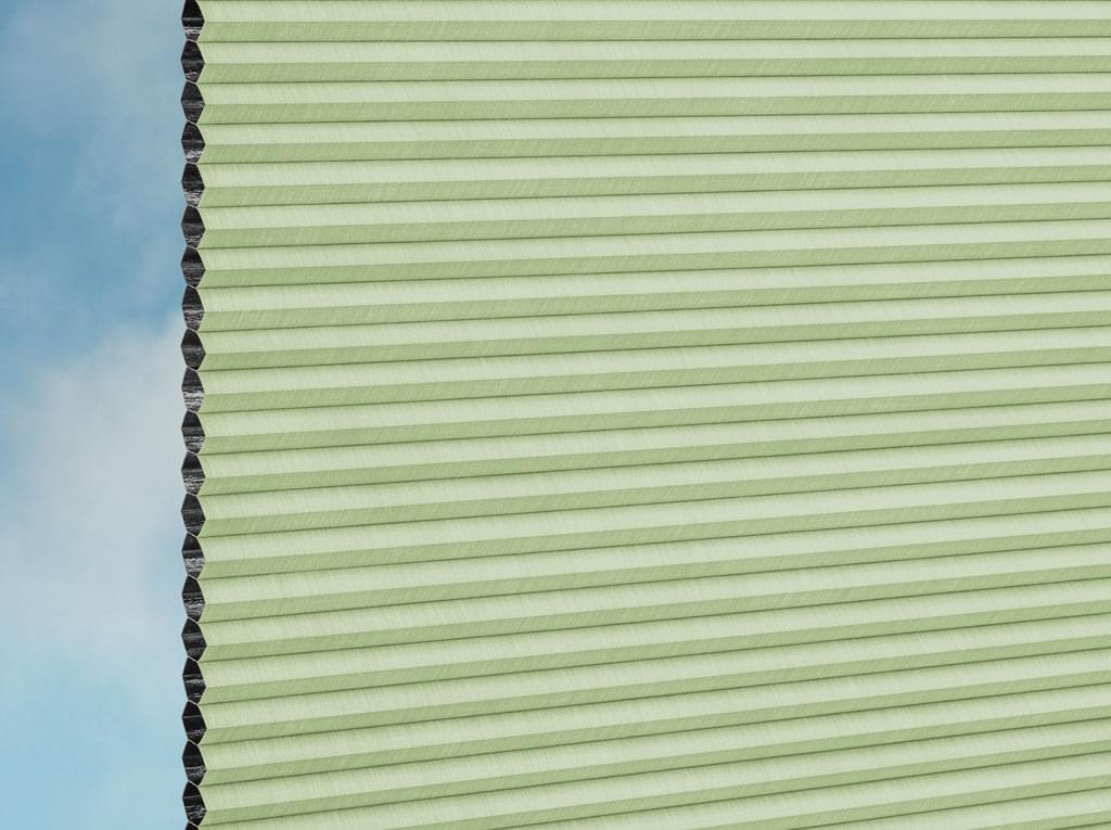 Nahaufnahme von DUETTE® Fixé Elan Dark (4.3773) Grüner Zellwabenschirm von Duetteshop mit hellgrünen Falten und schwarzem Rand vor blauem Himmel, der das strukturierte und isolierende Design hervorhebt.