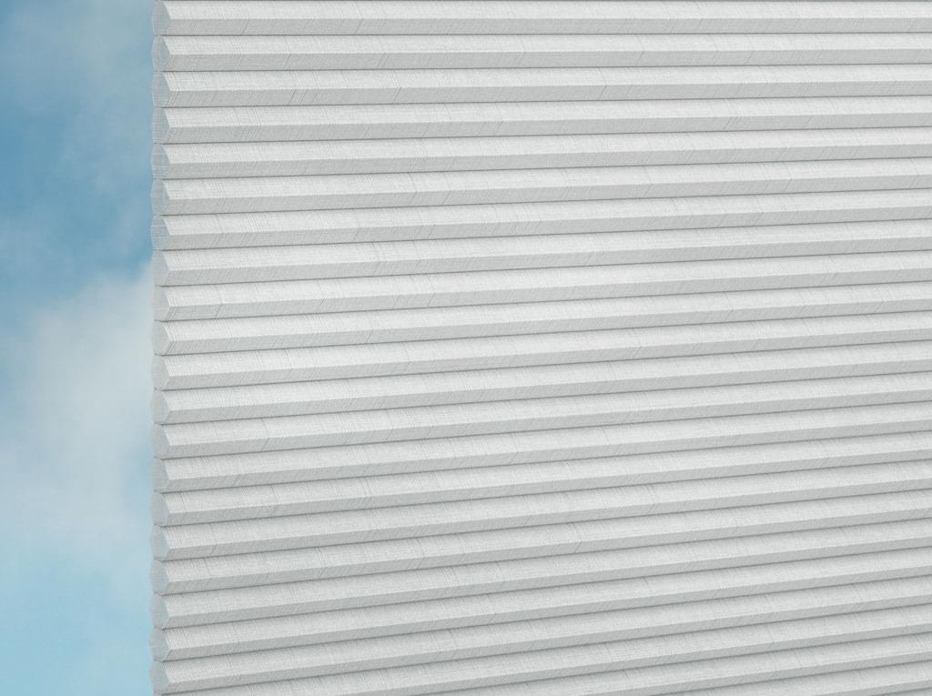 Nahaufnahme von DUETTE® Fixé Batiste (4.3352) Weiß von Duetteshop, mit weißer Wabenstruktur und eleganten Falten. Ein blassblauer Himmel und Wolken im Hintergrund unterstreichen den raffinierten Look dieser maßgefertigten Fensterbekleidung.