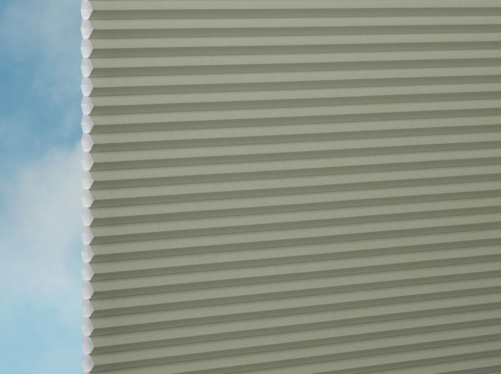 Nahaufnahme der DUETTE® Fixé Royale (4.3836) Grün Jalousie von Duetteshop, die ein Fenster mit blauem Himmel und weißen Wolken im Hintergrund teilweise verdeckt.